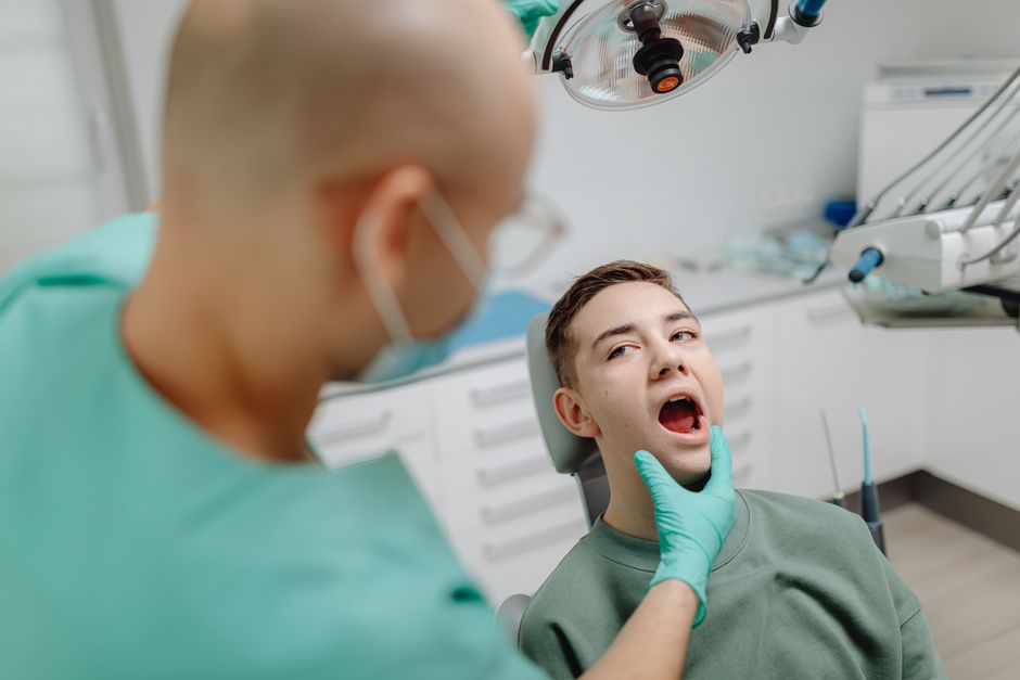 Dentist examining a young male patient's teeth during a dental appointment.