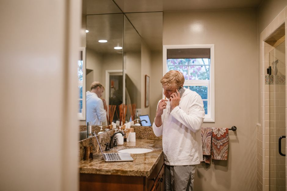 Man multitasking in bathroom, brushing teeth while on phone, reflecting daily routine.