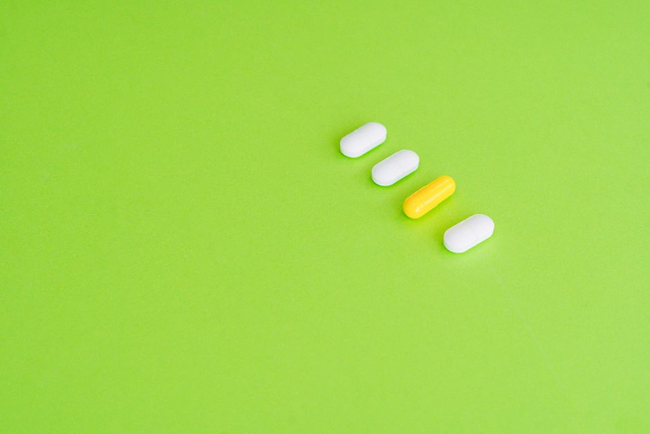 A row of white and yellow capsules on a green surface symbolizing medicine concept.