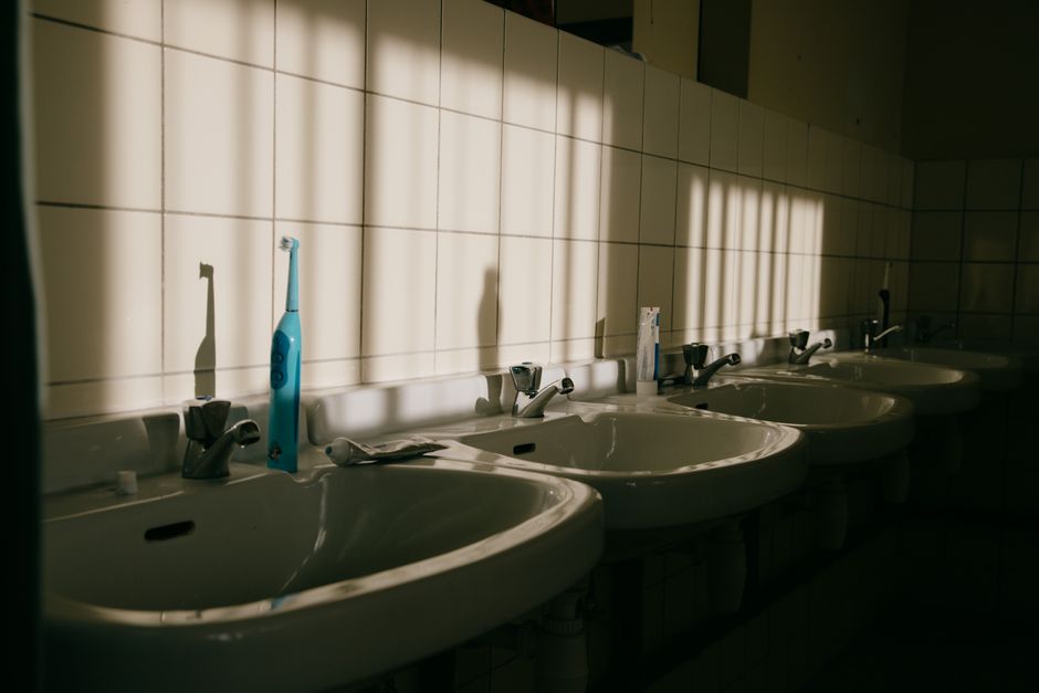 A row of bathroom sinks illuminated by sunlight, casting unique shadows on a tiled wall.