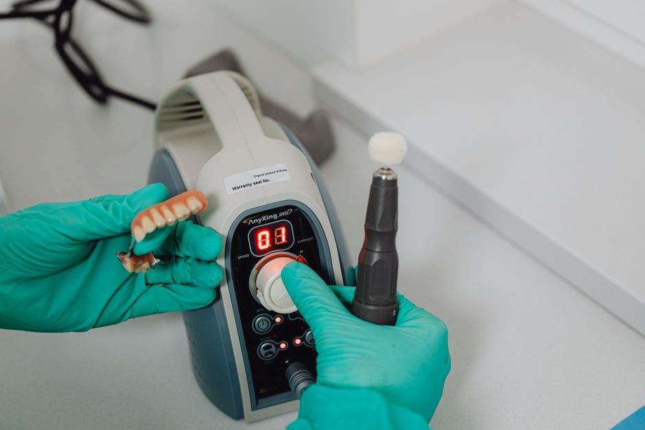 Close-up of dental technician's hands working with denture and medical machine in a lab.
