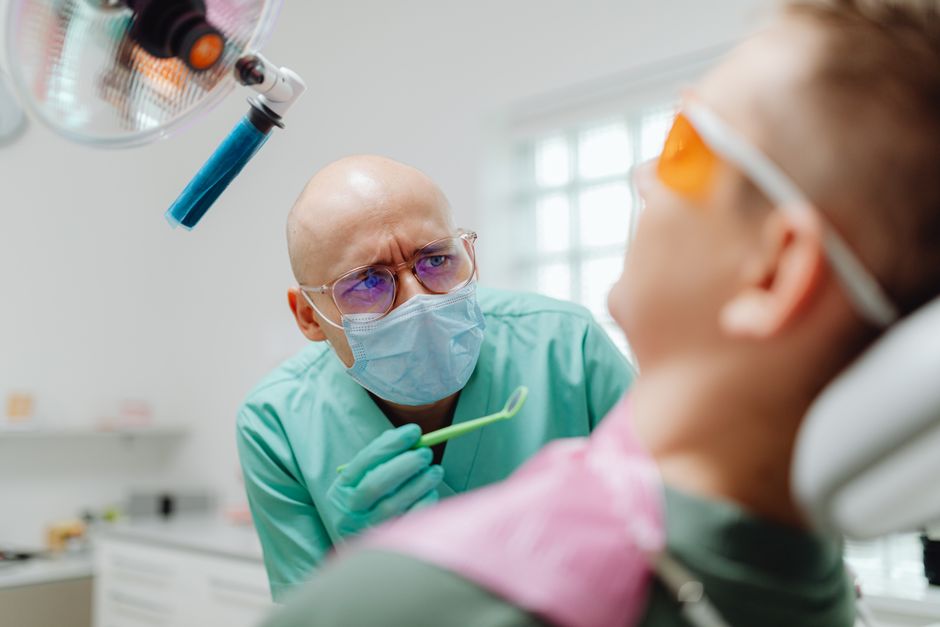 A bald dentist wearing eyeglasses examines a patient in a modern dental clinic.