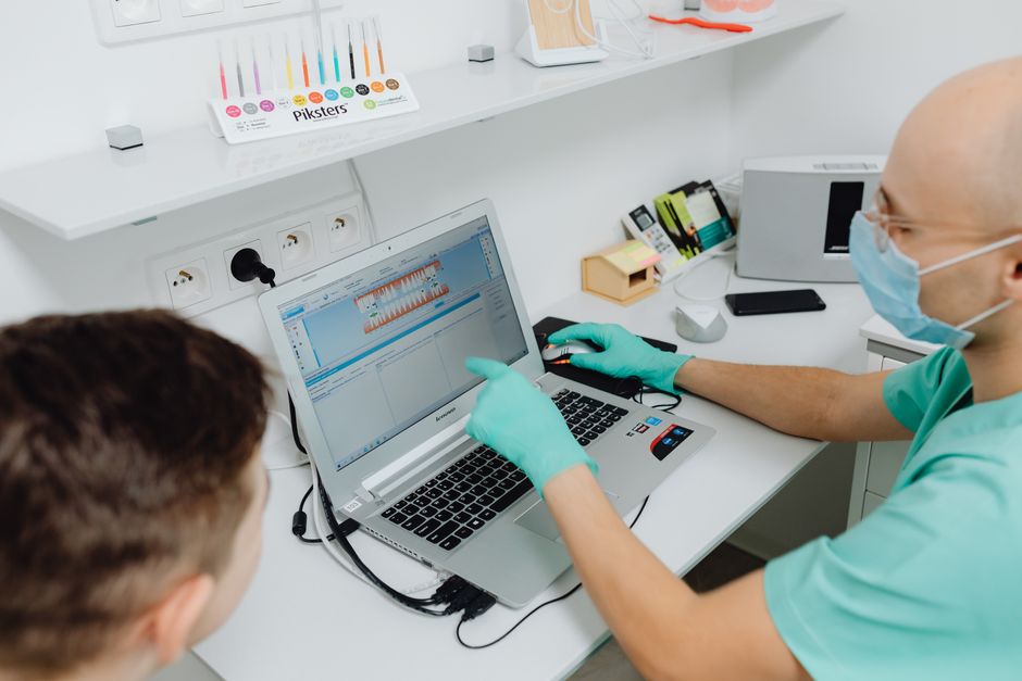Dentist explaining dental diagnosis to a patient using a laptop in a modern clinic.