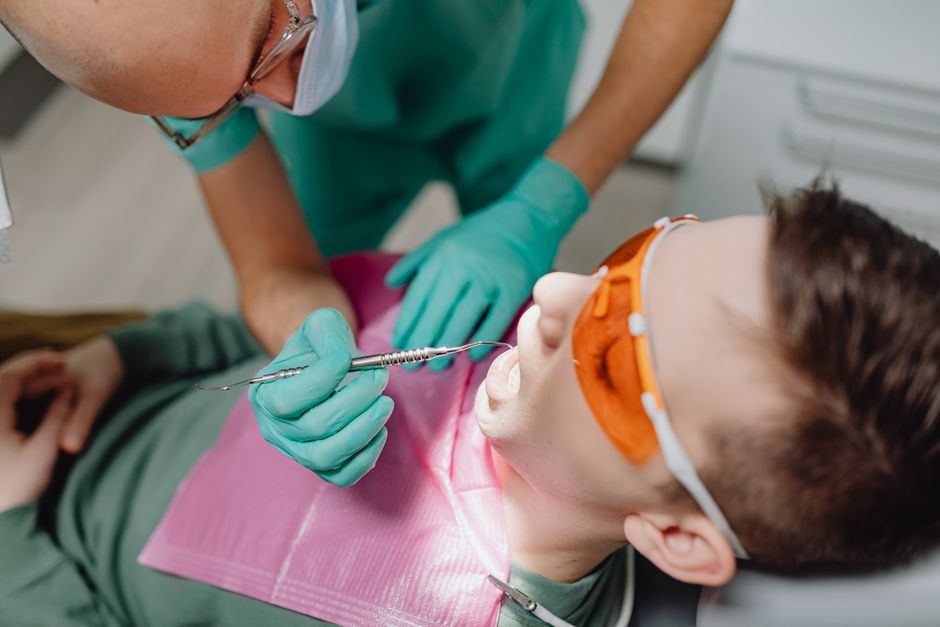 Dentist conducting a dental examination with patient using tools and protective eyewear.