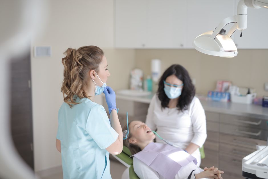 Professional female dentists in mask and gloves curing teeth of patient while working in dental room of modern clinic