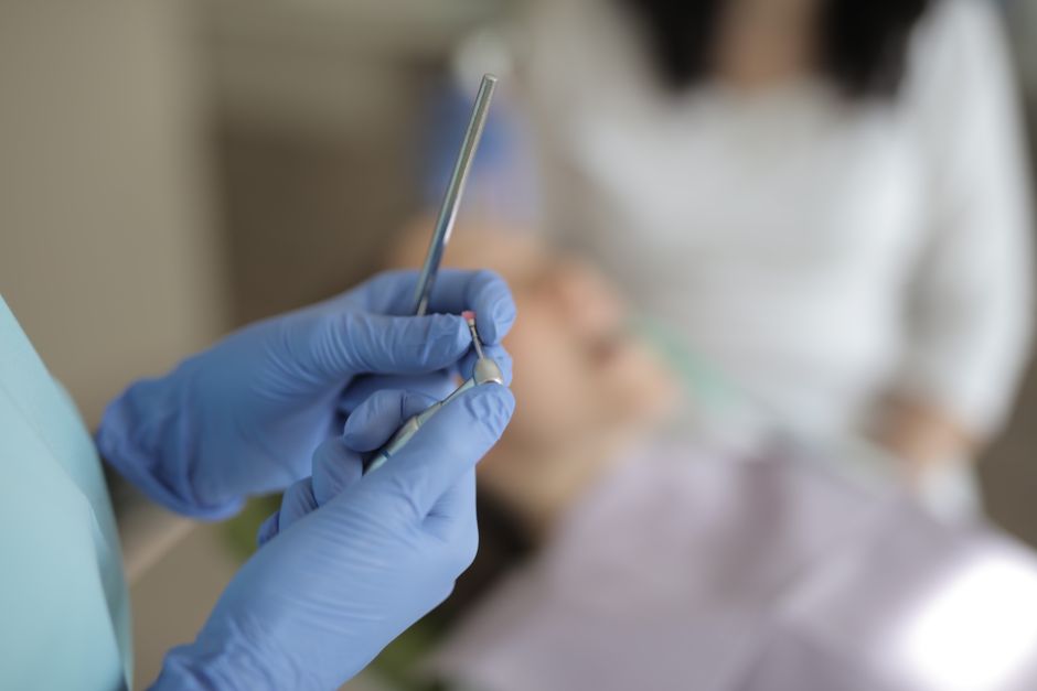 Unrecognizable crop dentist in latex gloves holding metal tools while standing in dental room during work with patient in modern clinic