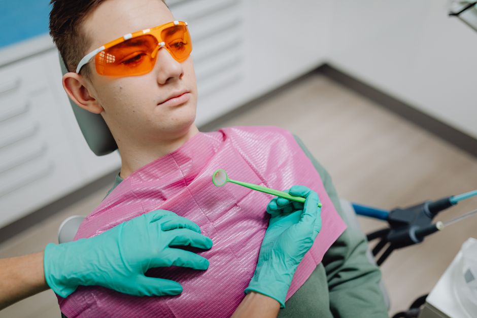 Patient in dental chair with sunglasses during examination by dentist wearing gloves.