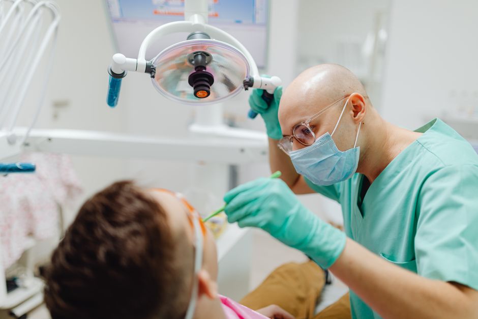 A dentist in green scrubs treating a patient under dental light in a clinic.
