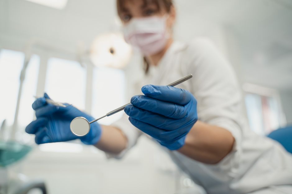 A dentist wearing blue gloves holds dental tools in a clinic setting, focused on dental care.