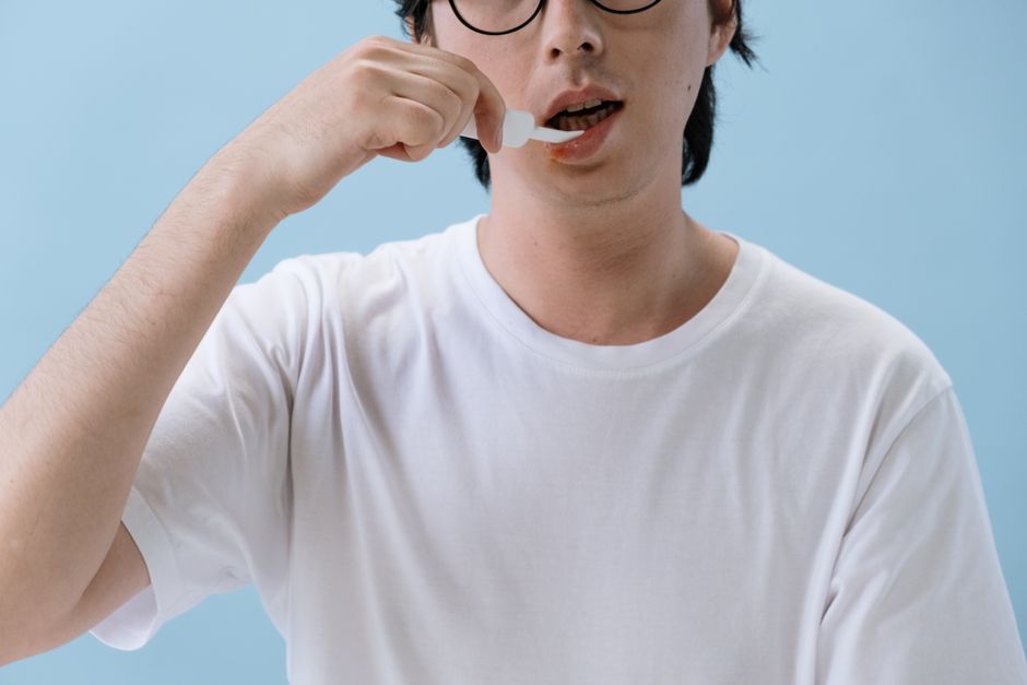 Close-up of a person using a dropper to take medication against a blue background.