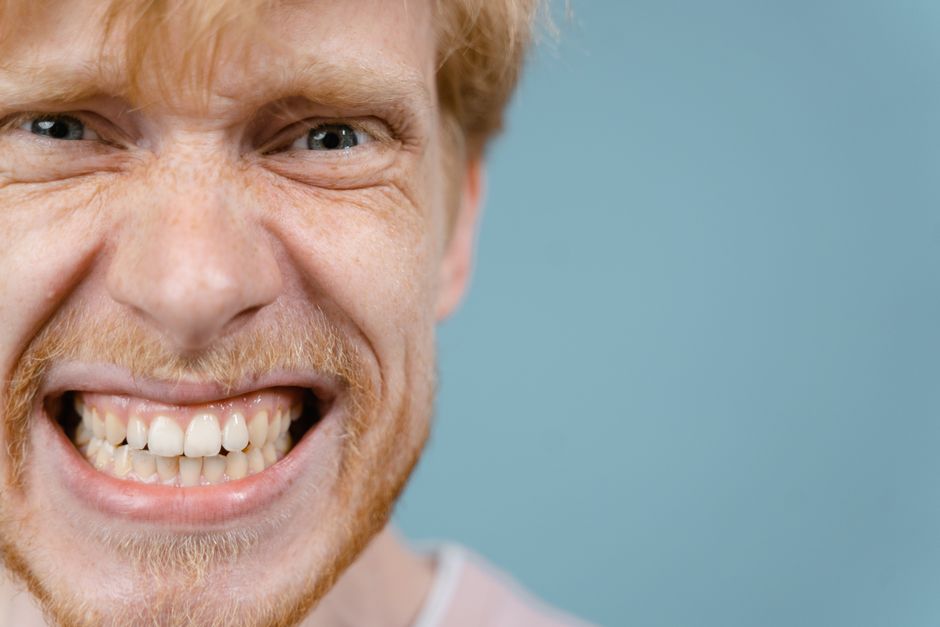 A close-up portrait of a man with a wacky and intense facial expression against a blue background.