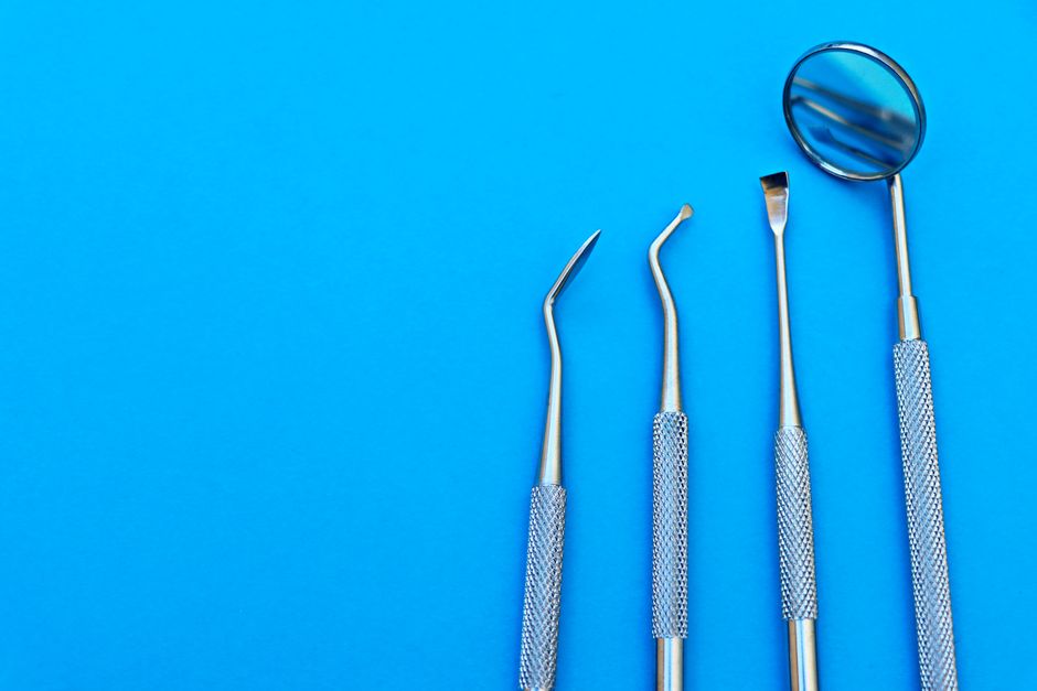 Close-up of stainless steel dental tools arranged on a bright blue surface, showcasing various instruments.