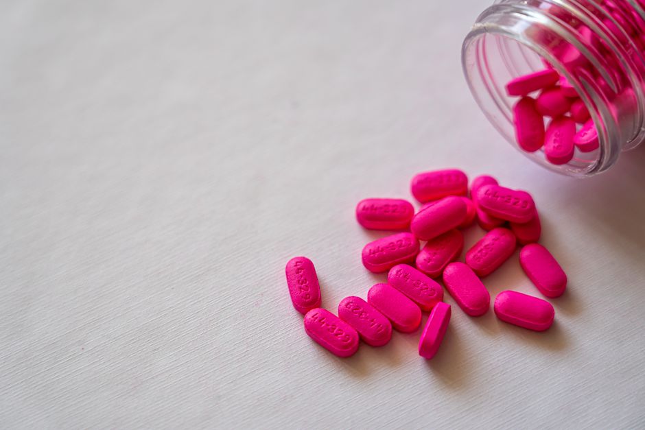 Pink pills spilling from a glass bottle onto a surface, highlighting pharmaceutical care and medication.