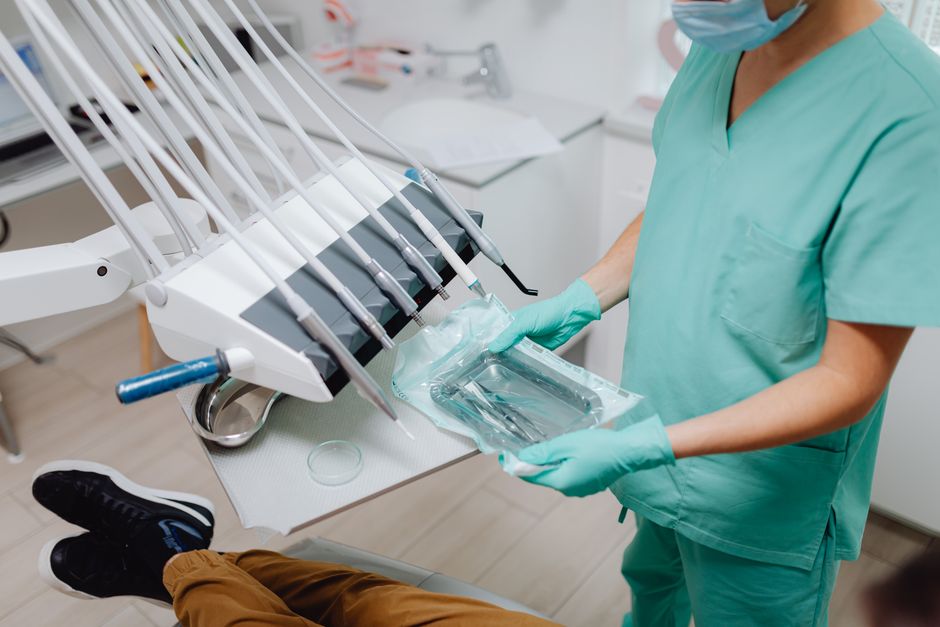 A dental professional in scrubs prepares sterile instruments for a procedure.