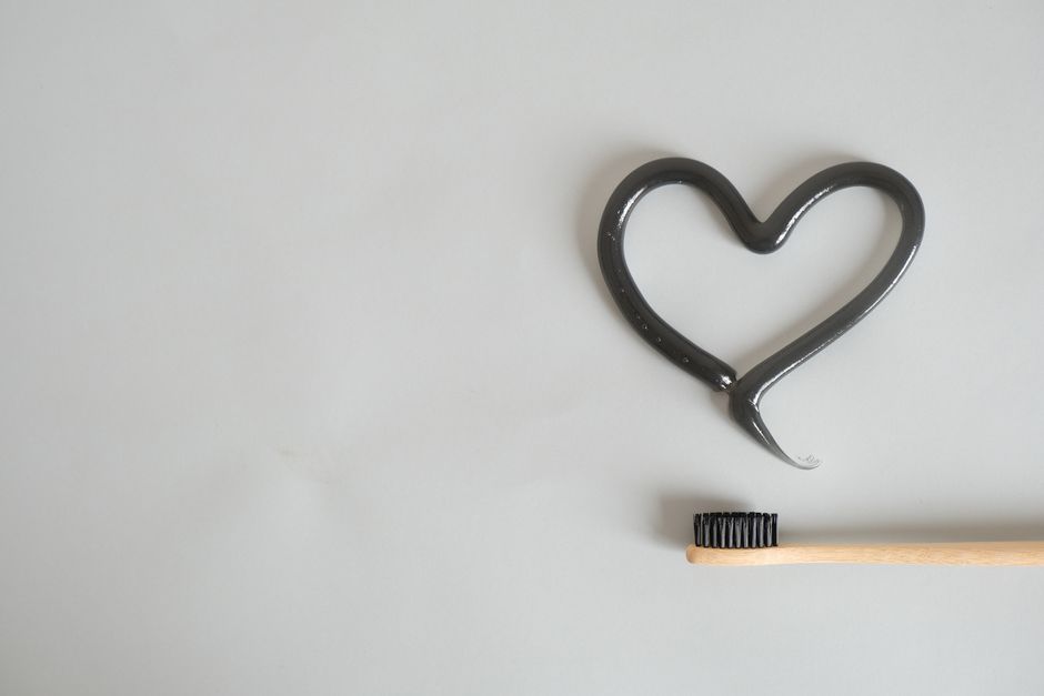 Charcoal toothpaste shaped as a heart with bamboo toothbrush on gray background. Ideal for eco-friendly dental care imagery.
