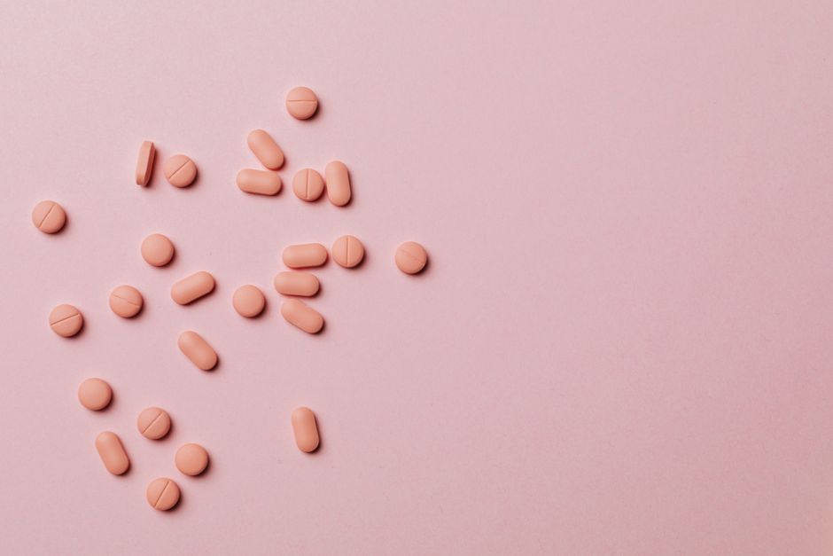 Flat lay of pink pills scattered on a pink background, conveying healthcare themes.