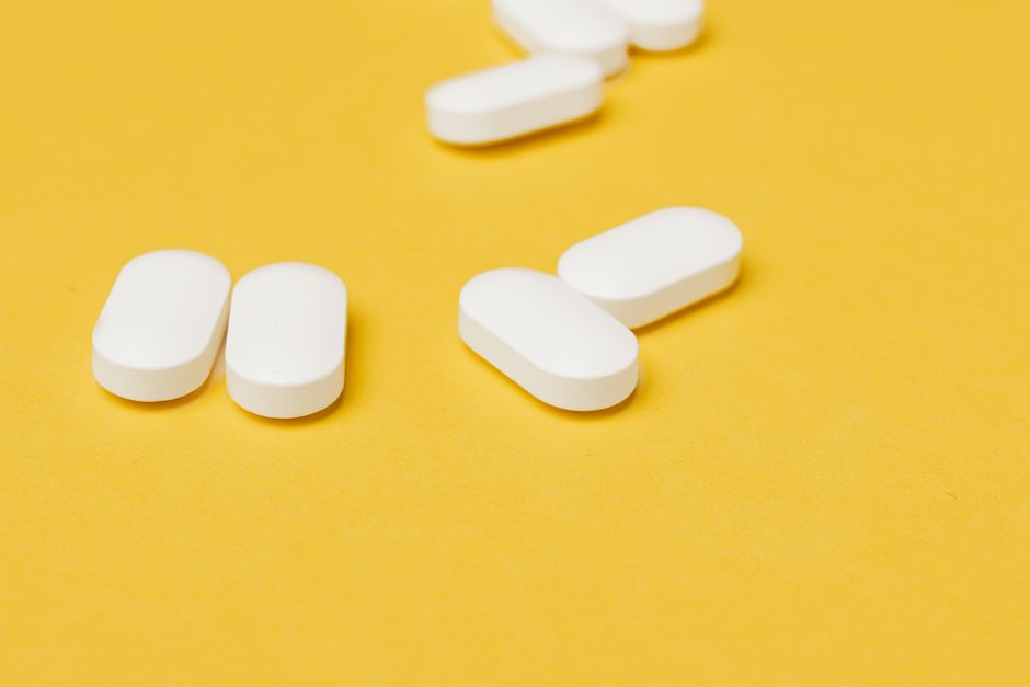 Set of medical white ellipse shaped pills placed in disorder on bright yellow background