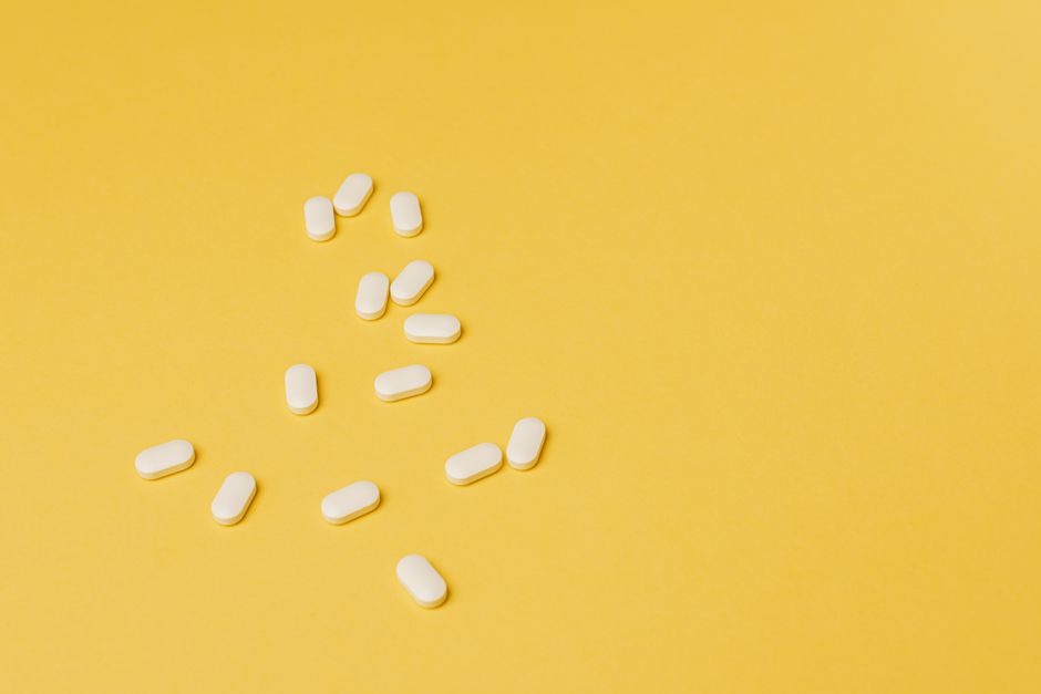 From above of small white ellipse shaped pills of same size randomly placed on bright yellow background