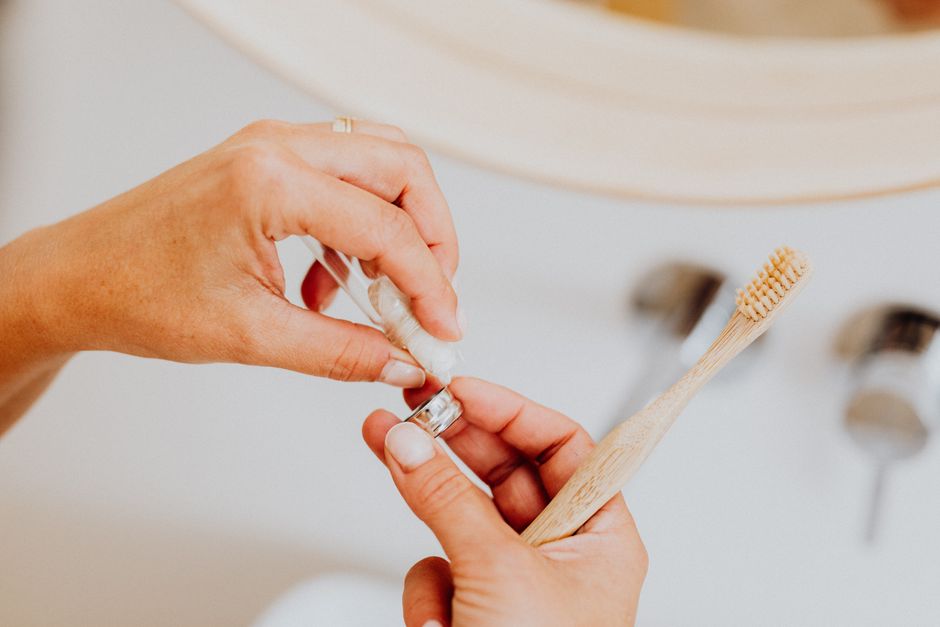 Adult hand applying toothpaste on an eco-friendly toothbrush indoors.