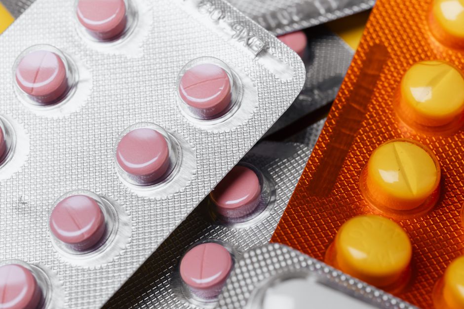 From above closeup mix of various multicolored round pills of different sizes in plastic blister packs under bright light