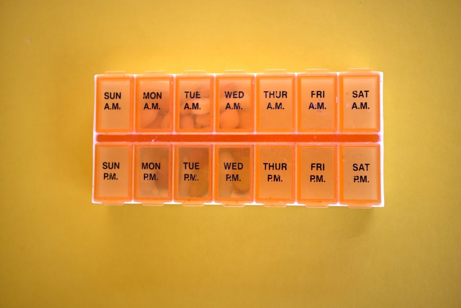 Orange pill organizer for daily medication with AM/PM compartments on a yellow backdrop.