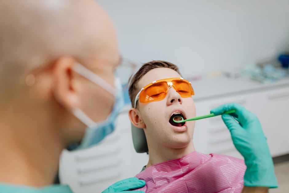 Teenager in dental clinic undergoing dental examination with dentist wearing protective gear.