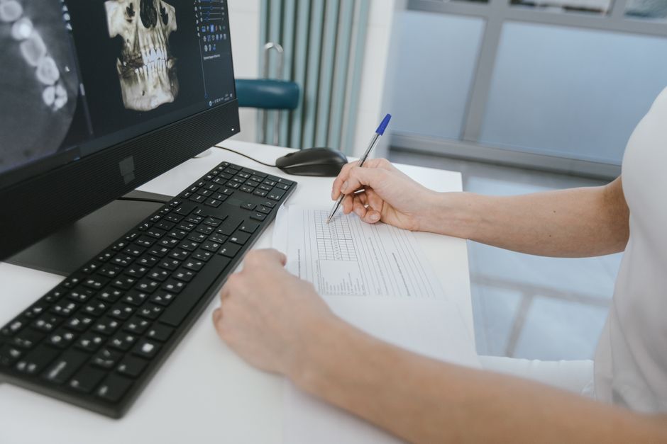 Close-up of a healthcare worker analyzing x-ray results and taking notes on a computer desk.