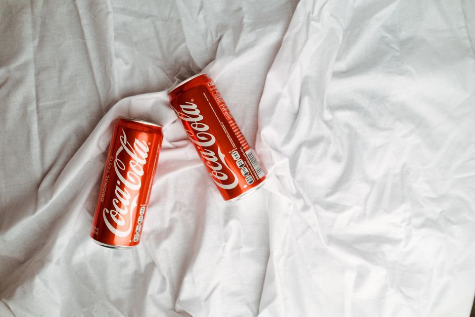 Two Coca Cola cans placed on a crumpled white textile, showcasing a classic beverage design.