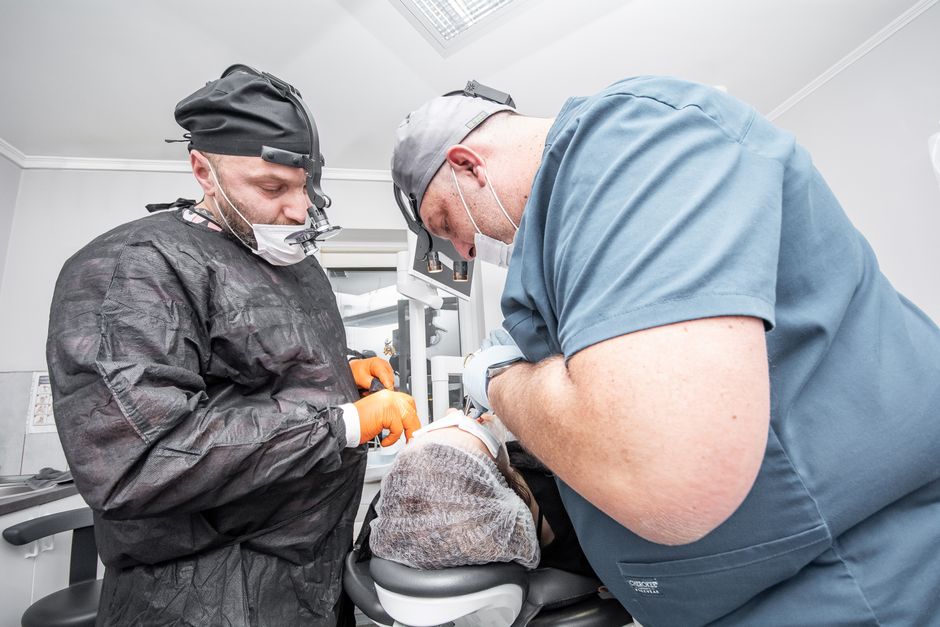 Dentists in surgical scrubs and masks performing a dental procedure in a modern clinic.