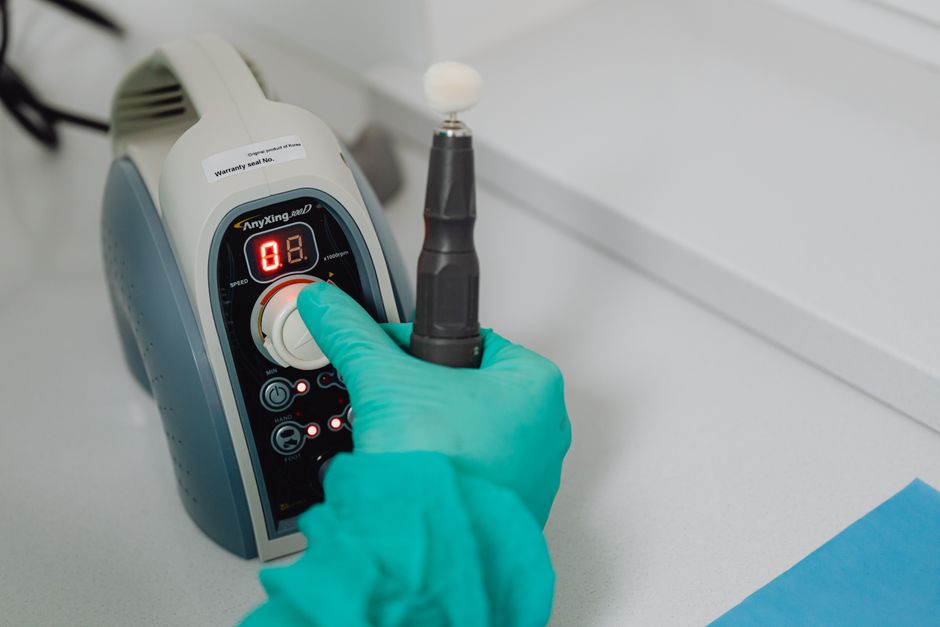 Gloved hand operating dental tool with digital display in a clinical setting.