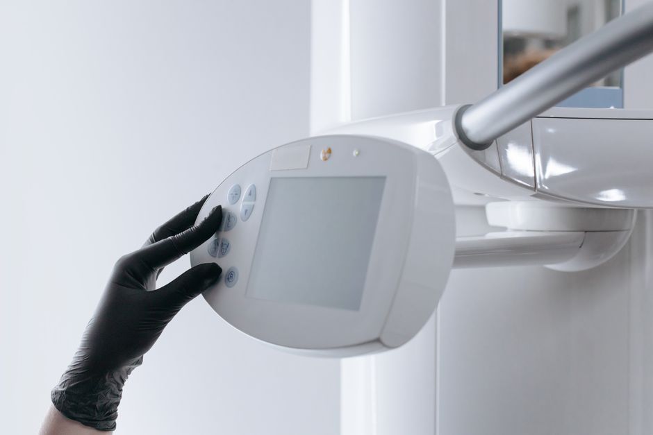 Close-up of gloved hand operating dental x-ray machine in clinical setting.