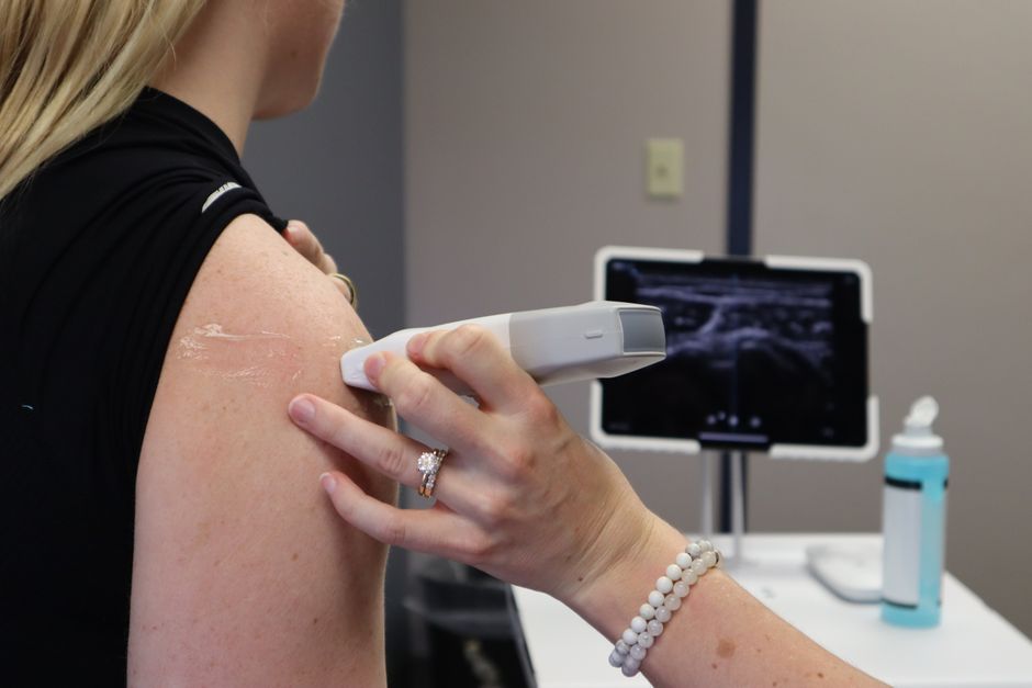 Healthcare professional conducting an ultrasound on a shoulder injury in a medical office.