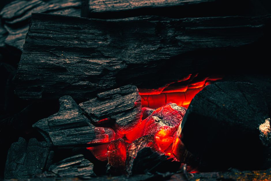 Close-up view of glowing charcoal embers with dark wood, creating a warm and dramatic effect.