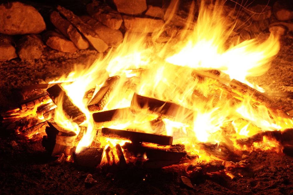 Close-up view of a vibrant campfire burning brightly at night with logs and stones.