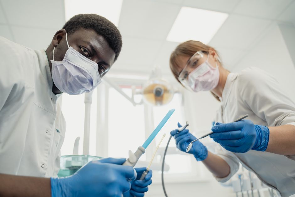 Dental professionals in masks and gloves working with tools in a clinical setting.
