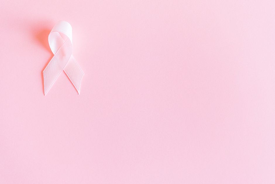 A pink ribbon on a soft pink background symbolizing breast cancer awareness and solidarity.