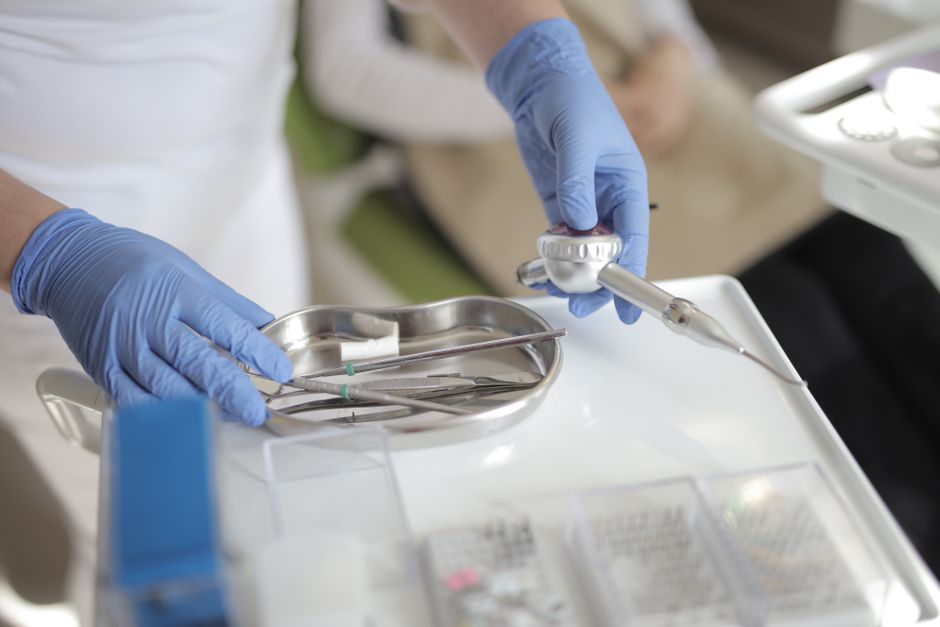 Anonymous crop doctor in latex gloves taking metal medical instruments from table while preparing for treatment in modern clinic