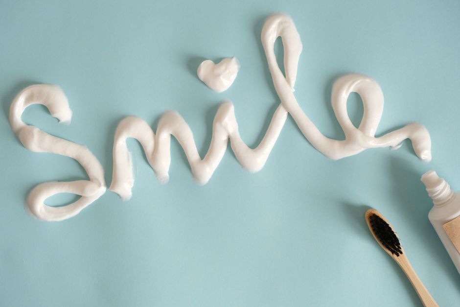 Toothpaste spelling 'Smile' on turquoise surface with toothbrush.