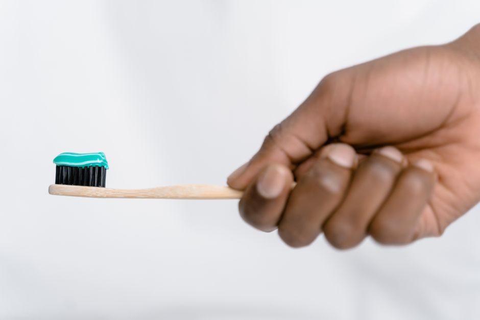 Hand holding a bamboo toothbrush with green toothpaste, focusing on oral hygiene.