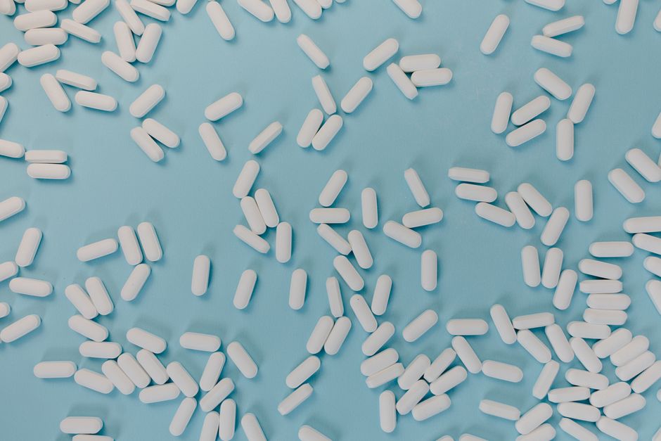 Top view of scattered white pills on a blue surface, representing healthcare and medicine.