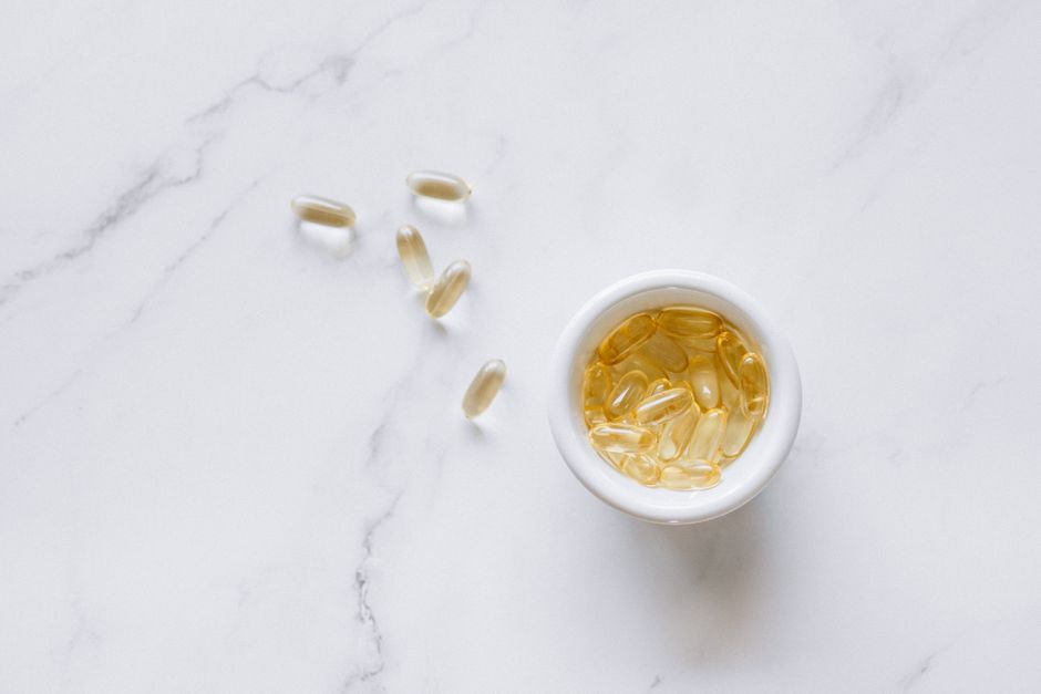 Top view of scattered capsules and a bowl on a marble surface, minimalistic setup.