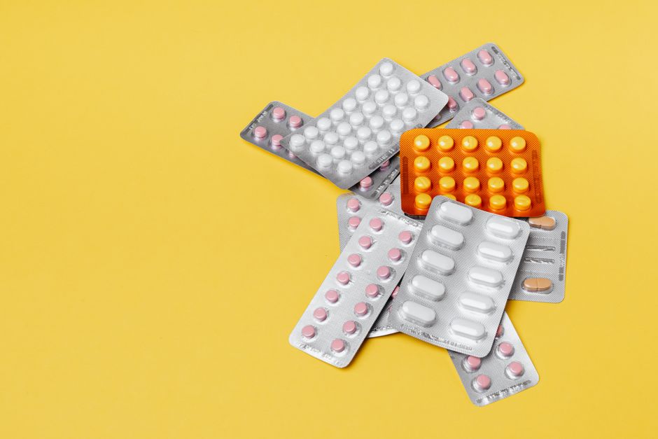 From above of various medication blister packs of different color and shape on yellow background