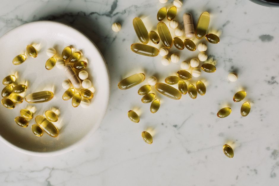Assorted pills and vitamins displayed on a marble surface with natural lighting.