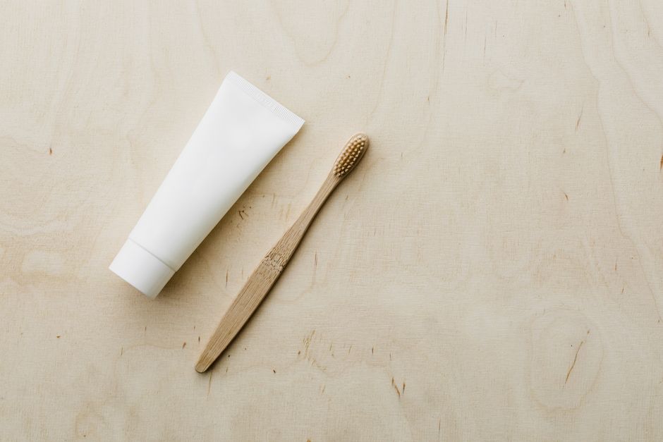 Overhead view of white mockup toothpaste tube and light brown bamboo toothbrush placed on wooden copy space surface