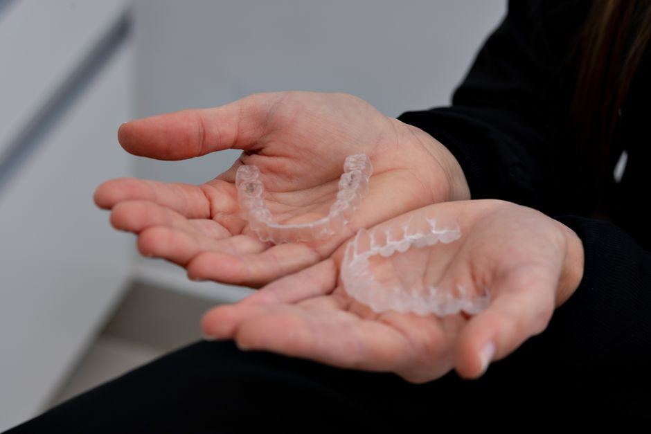 Close-up of hands holding clear dental aligners in a dental clinic setting.