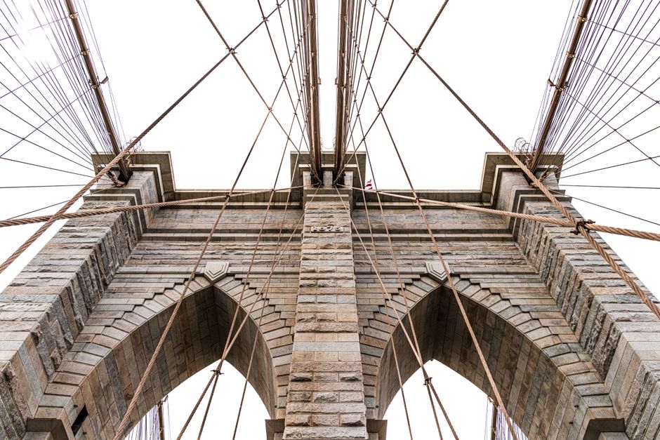 Low-angle view of the iconic Brooklyn Bridge's architectural details and cables in New York City.