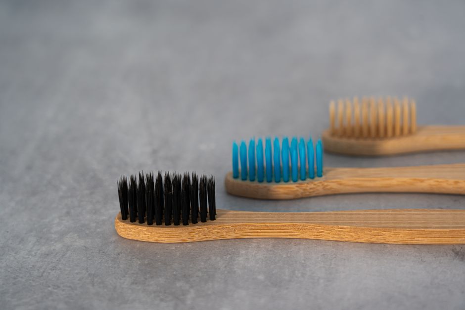 Close-up of three eco-friendly bamboo toothbrushes with colored bristles on a gray surface.