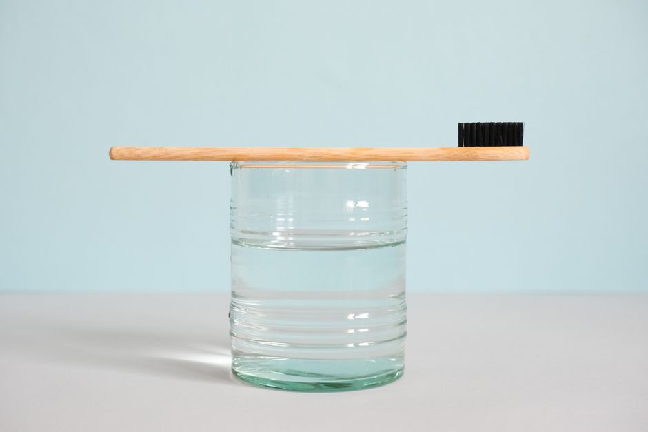 Minimalist image of a bamboo toothbrush atop a glass of water, emphasizing sustainable hygiene.