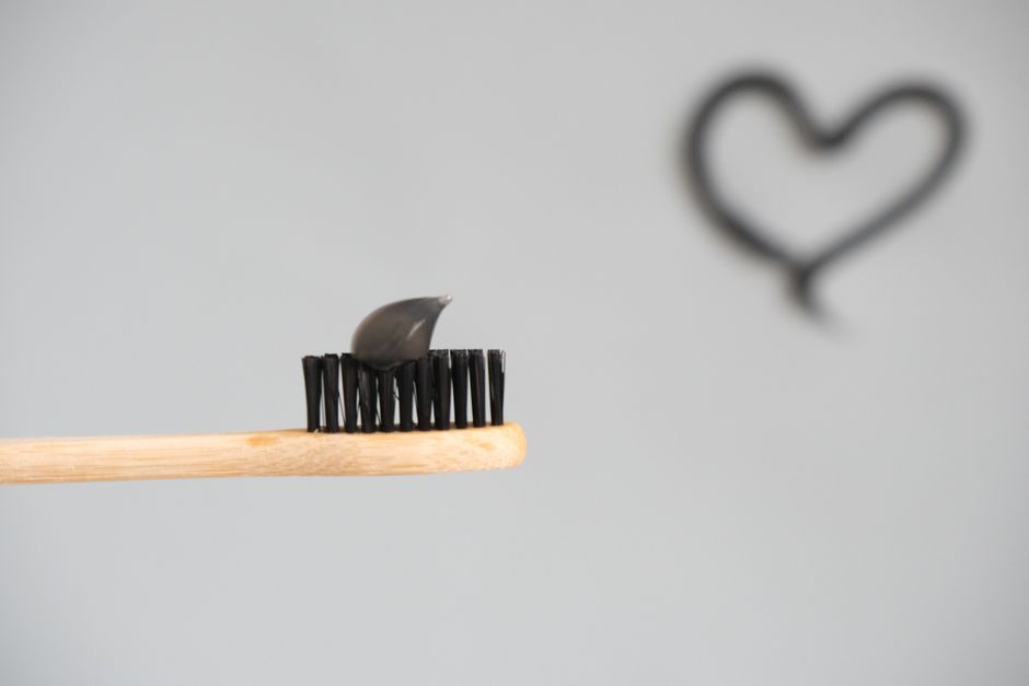 Close-up of a bamboo toothbrush with charcoal toothpaste on a neutral background.